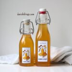 To flasker gløggsirup med påsatte etiketter - klar til brug. Æblegløggekstrakt og koncentreret gløggsirup (1:1) - den perfekte julegave! 🍎✨ Lær hvordan du laver en hurtig gløggekstrakt og en koncentreret gløggsirup, der kan bruges til alt fra klassisk gløgg og gløggspritz til te, sodavand og det søde køkken – både varm og kold. Find opskriften, masser af anvendelsesmuligheder og gratis etiketter til print på danishthings.com © Christel Parby #DanishThings #gløggsirup #julesirup #gløggekstrakt #æblegløggekstrakt #hjemmelavetgave #æblegløgg #juleopskrifter #julehygge #gløgg #værtindegave #julesmag #opskrift #drinksirup