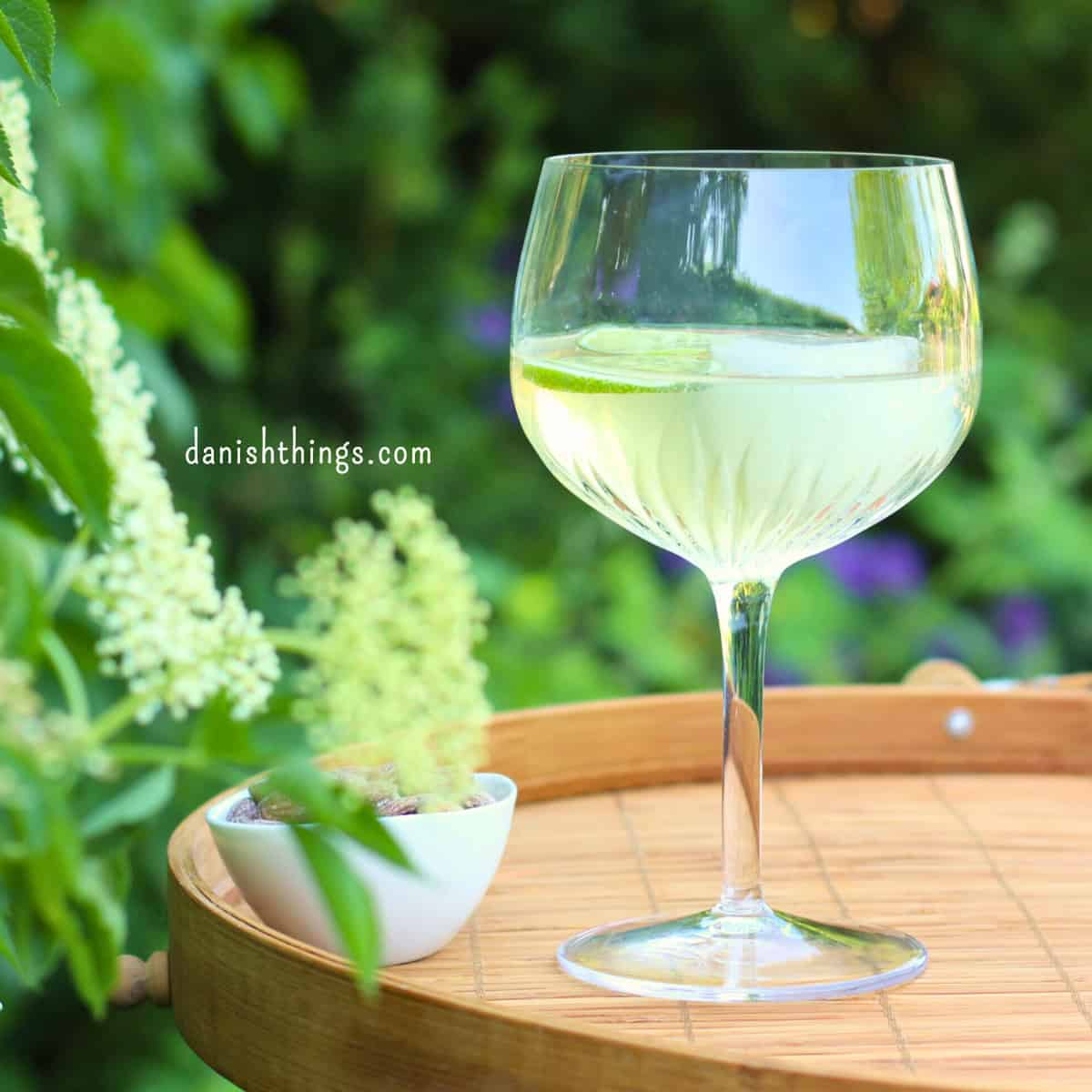 Glas med hyldeblomstdrink på en bakke. Lav en forfriskende hyldeblomstmocktail med kun 4 ingredienser - hvor den ene er isterninger. Tilsæt hjemmelavet hyldeblomstvodka - eller gin, og du har en sommerfrisk cocktail. Find opskriften, variationer og inspiration til sommerens drinks på danishthings.com © Christel Parby #DanishThings #hyldeblomst #hyldeblomstmocktail #hyldeblomstcocktail #mocktail #cocktail #vodkatonic #hyldeblomstvodka #sommerdrink #SpisSommeren