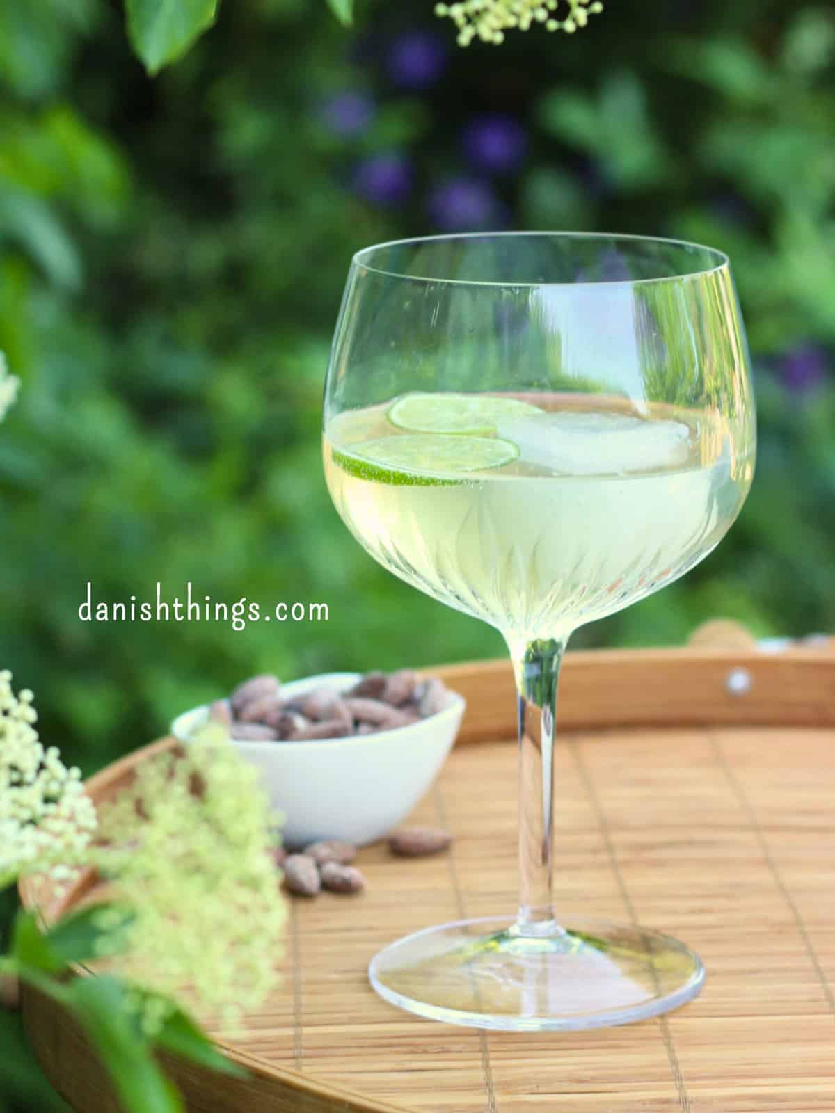 Hyldeblomstcocktail eller mocktail på en bakke udendørs. Lav en forfriskende hyldeblomstmocktail med kun 4 ingredienser - hvor den ene er isterninger. Tilsæt hjemmelavet hyldeblomstvodka - eller gin, og du har en sommerfrisk cocktail. Find opskriften, variationer og inspiration til sommerens drinks på danishthings.com © Christel Parby #DanishThings #hyldeblomst #hyldeblomstmocktail #hyldeblomstcocktail #mocktail #cocktail #vodkatonic #hyldeblomstvodka #sommerdrink #SpisSommeren