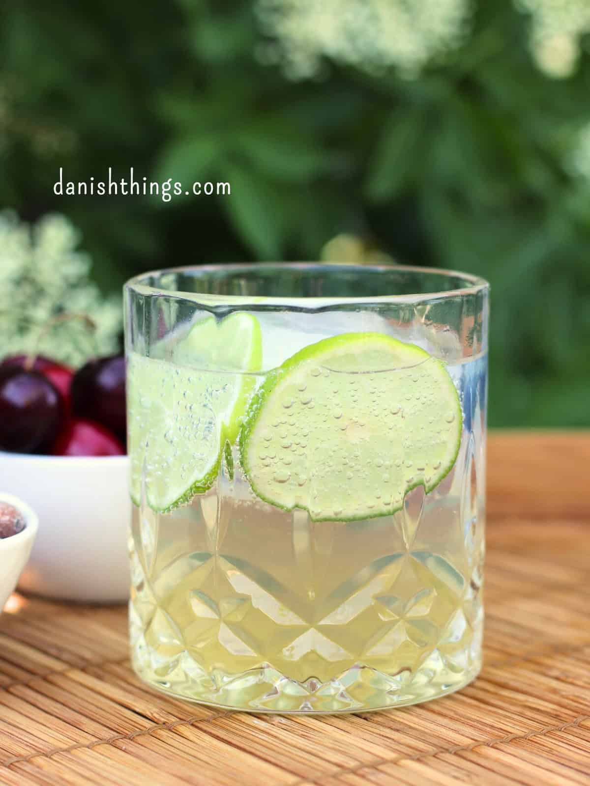 Hyldeblomstcocktail eller mocktail på en bakke udendørs. Lav en forfriskende hyldeblomstmocktail med kun 4 ingredienser - hvor den ene er isterninger. Tilsæt hjemmelavet hyldeblomstvodka - eller gin, og du har en sommerfrisk cocktail. Find opskriften, variationer og inspiration til sommerens drinks på danishthings.com © Christel Parby #DanishThings #hyldeblomst #hyldeblomstmocktail #hyldeblomstcocktail #mocktail #cocktail #vodkatonic #hyldeblomstvodka #sommerdrink #SpisSommeren