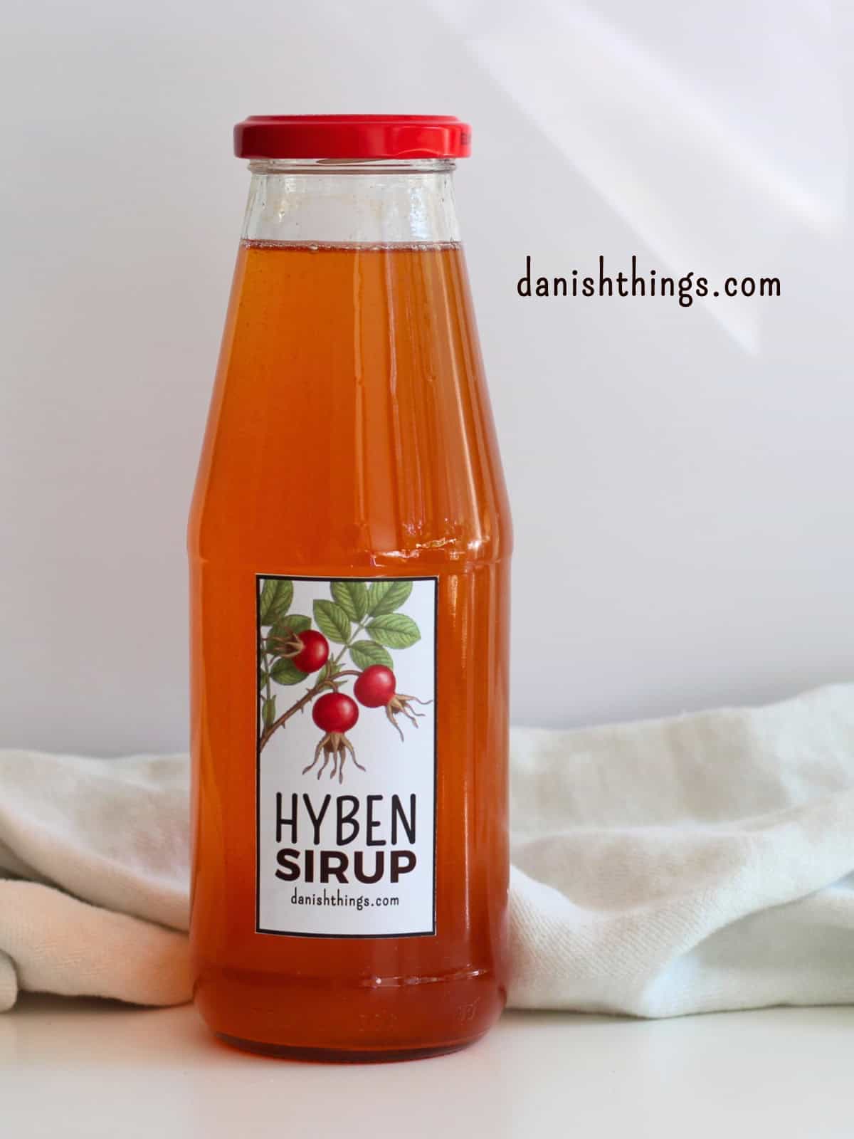 Hybenekstrakt og hybensirup af hele hyben – uden at fjerne kerner Færdig hybensirup på flaske, klar til brug i drikke, desserter og madlavning. Lav sirup af hele hyben uden at rense for kerner og hybenhår. Find hele opskriften med trin-for-trin-fremgangsmåde på danishthings.com. © Christel Parby #DanishThings #hybensirup #hybenekstrakt #hjemmelavetsirup #etiketter #hyben