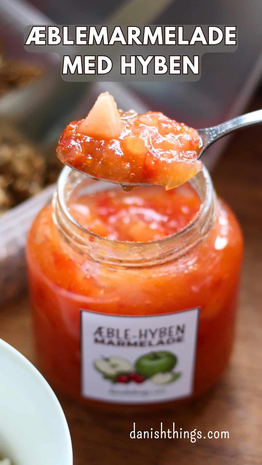Æblemarmelade med hyben - få en 2-i-1 opskrift, tips og gratis etiketter Ske med æble-hybenmarmelade over et åbent glas med tydelige lyse æblestykker. Her kan du se æblestykkerne tydeligt i æble-hybenmarmeladen. Kog marmeladen mindre ud, hvis du gerne vil bevare mere struktur, eller kog den længere, hvis du vil have en blødere marmelade eller mos. Få opskriften og tips til både æbler og hyben på danishthings.com © Christel Parby #DanishThings #æblemarmelade #hybenmarmelade #marmeladeopskrift #hjemmelavetmarmelade #hyben #æbler
