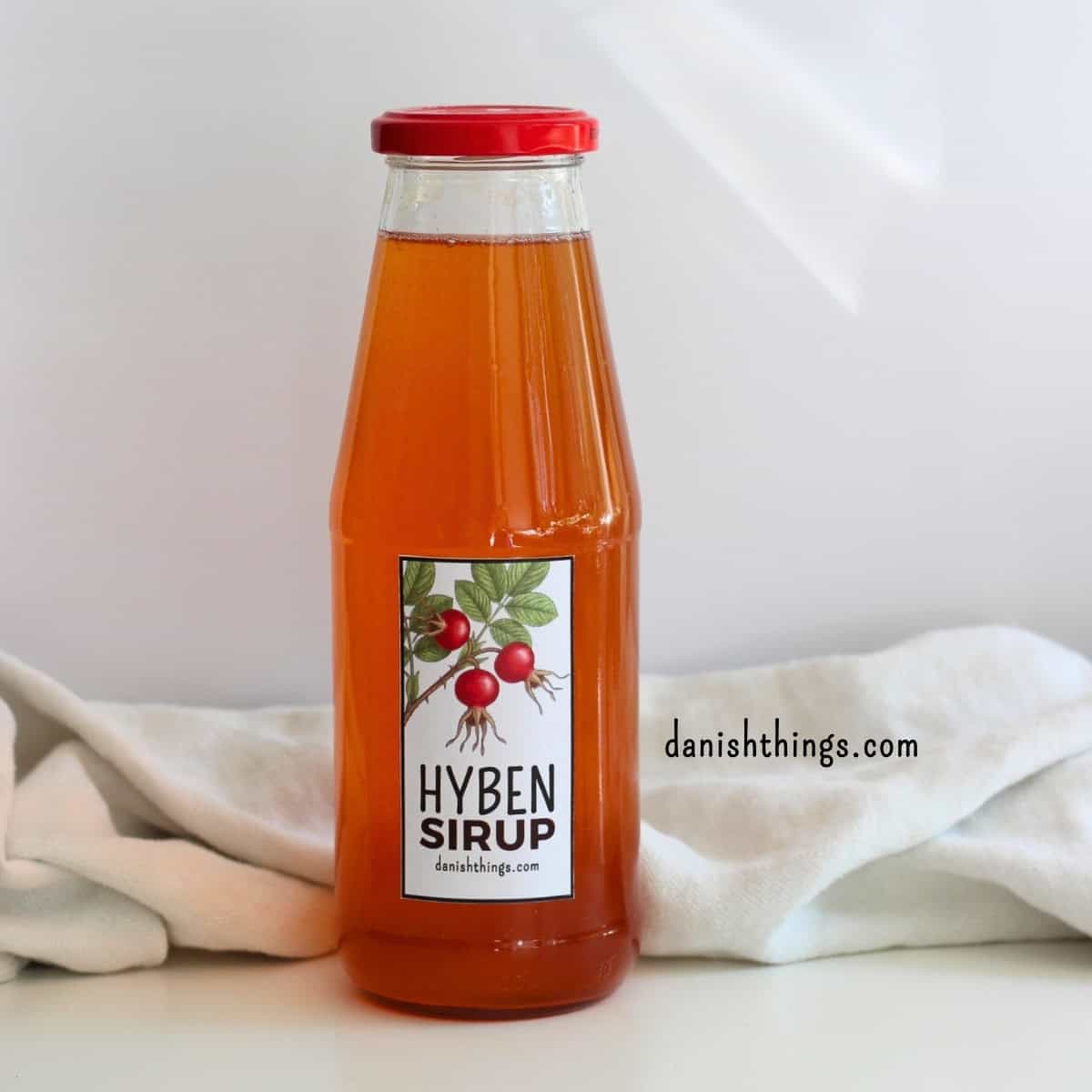Hybenekstrakt og hybensirup af hele hyben – uden at fjerne kerner Hjemmelavet hybensirup på flaske – sirup lavet af hyben fra rynket rose (Rosa rugosa) får en smuk orange farve. Lav sirup af hele hyben uden at rense for kerner og hybenhår. Find opskriften på danishthings.com. © Christel Parby #DanishThings #hybensirup #hjemmelavetsirup #hyben