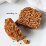 Overskåret bananmuffin med valnødder og crumble på en hvid tallerken. Den gennemskårne muffin viser den bløde, saftige krumme. Find opskriften på bananmuffins med valnødder på Danish Things © Christel Parby #DanishThings #bananmuffins #banan #muffins #bananopskrift #muffinmetoden #valnøddecrumble #valnødder #brunebananer #crumble #stopmadspild