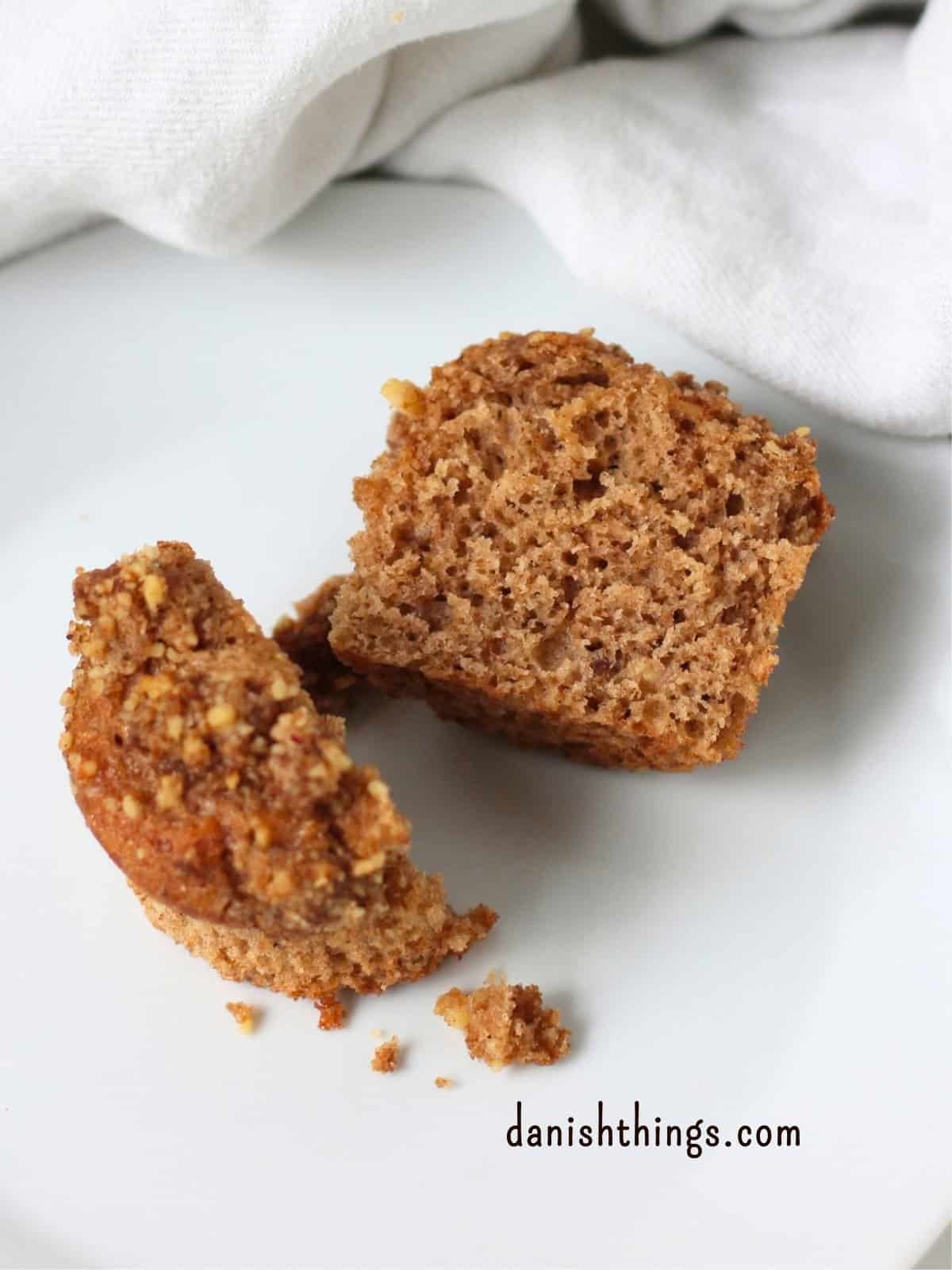 Overskåret bananmuffin med valnødder og crumble på en hvid tallerken. Den gennemskårne muffin viser den bløde, saftige krumme. Find opskriften på Danish Things © Christel Parby #DanishThings #bananmuffins #banan #muffins #bananopskrift #muffinmetoden #valnøddecrumble #valnødder #brunebananer #crumble #stopmadspild