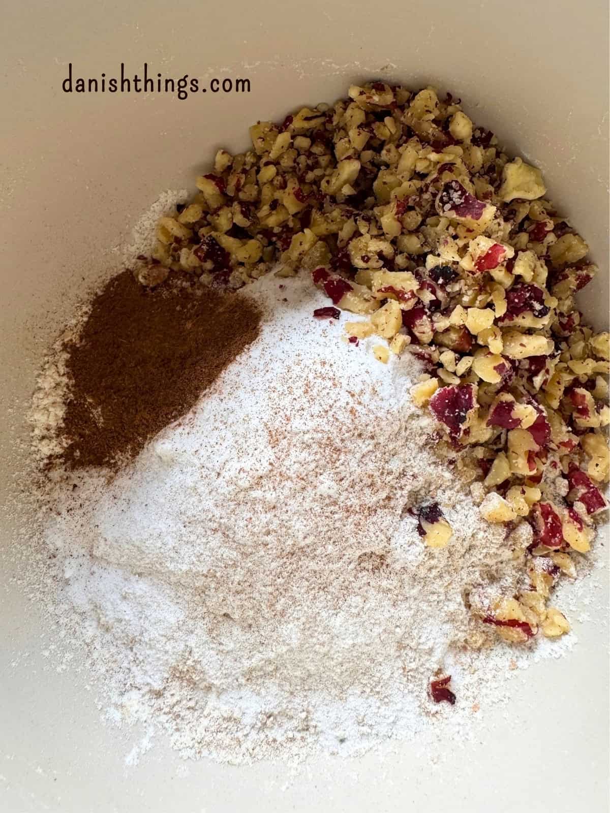 De tørre ingredienser til bananmuffins blandes i en skål. Hvedemel, fuldkornshvedemel, hævemidler, kanel og grofthakkede valnødder skal blandes, inden de våde ingredienser tilsættes. Find opskriften på Danish Things © Christel Parby #DanishThings #bananmuffins #muffins #bananopskrift #muffinmetoden #hjemmebag #valnødder #kanel #kagekrydderi #stopmadspild