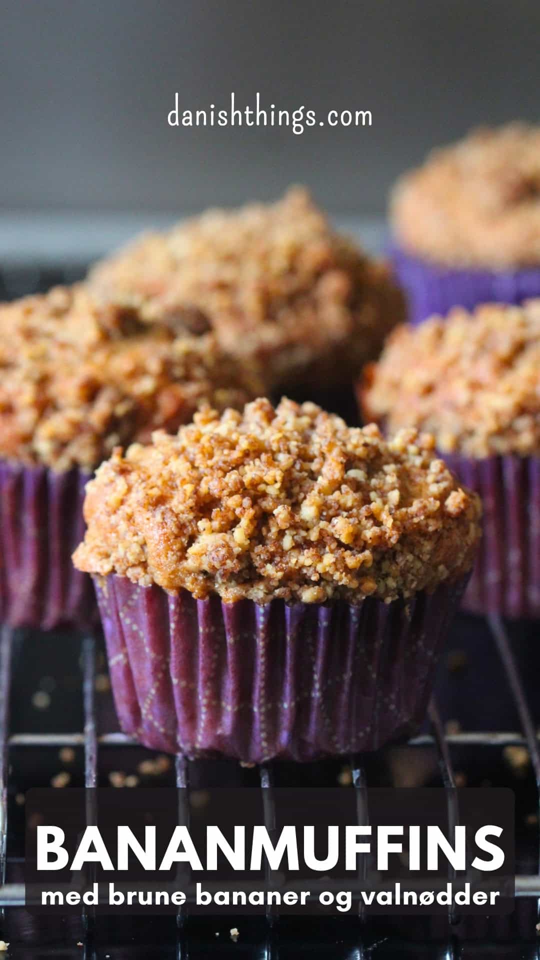 Flere friskbagte bananmuffins med sprød valnøddecrumble i lilla papirforme på en bagerist. Bananmuffins med brune bananer og valnødder – en nem opskrift med muffinmetoden, kanel og en sød crumble med kagekrydderi. Find opskriften på Danish Things © Christel Parby #DanishThings #bananmuffins #banan #muffins #bananopskrift #muffinmetoden #hjemmebag #valnøddecrumble #valnødder #brunebananer #kanel #kagekrydderi #crumble 