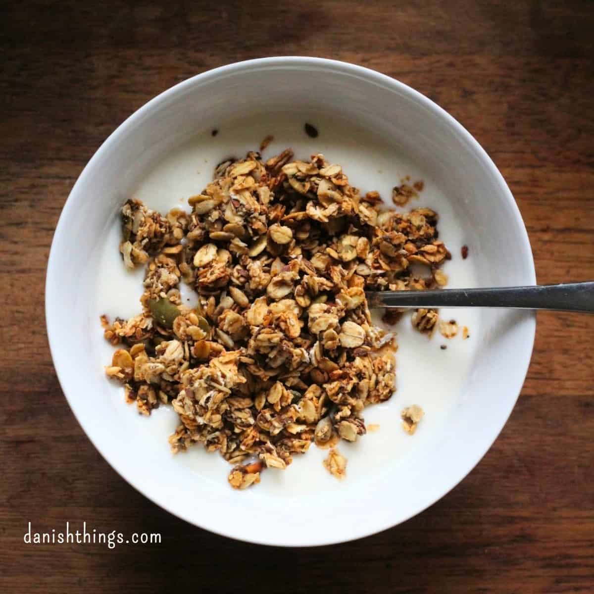 Sprød hverdagsgranola sødet med banan - granola uden tilsat sukker Skål med kefir toppet med sprød hjemmelavet hverdagsgranola på et mørkt træbord. Granolaen er sødet med banan og kan bruges til morgenmad, som snack eller som topping på yoghurt, grød og smoothie bowls. Få opskriften på danishthings.com © Christel Parby #DanishThings #granola #hverdagsgranola #banan #morgenmad