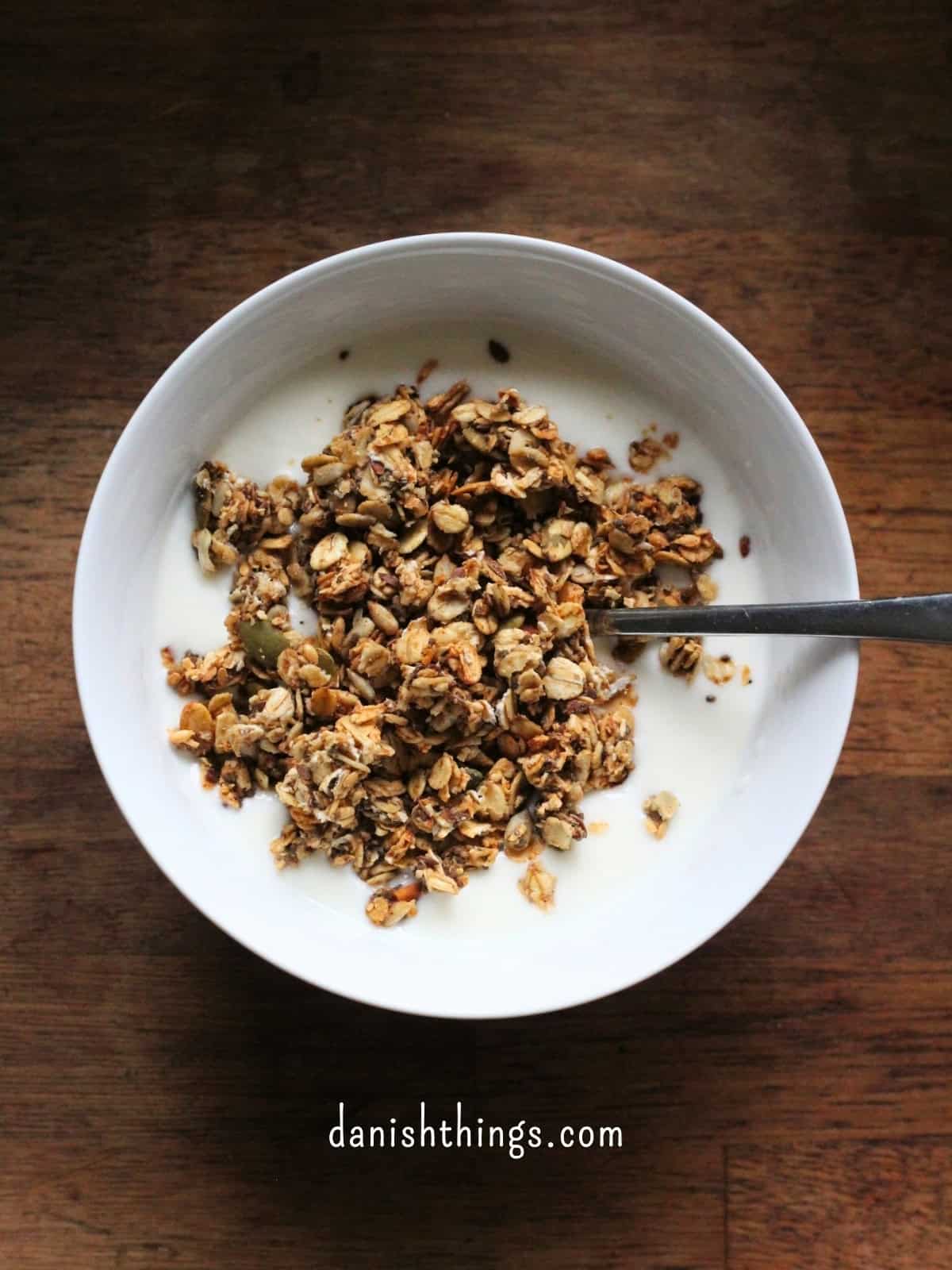 Sprød hverdagsgranola sødet med banan - granola uden tilsat sukker Skål med kefir toppet med sprød hjemmelavet hverdagsgranola på et mørkt træbord. Granolaen er sødet med banan og kan bruges til morgenmad, som snack eller som topping på yoghurt, grød og smoothie bowls. Få opskriften på danishthings.com © Christel Parby #DanishThings #granola #hverdagsgranola #banan #morgenmad