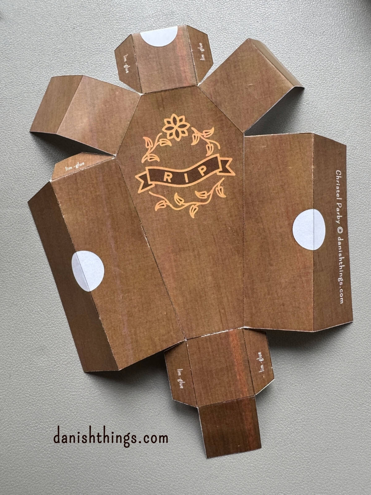 Et brunt kistelåg ligger udfoldet med synlige foldelinjer og udskæringer til lågets halvcirkler. Det farvede kisteprint skal foldes, så den brune side vender udad.
© Christel Parby · danishthings.com · #DanishThings #Halloweenkiste #Papirfoldning #GratisPrint