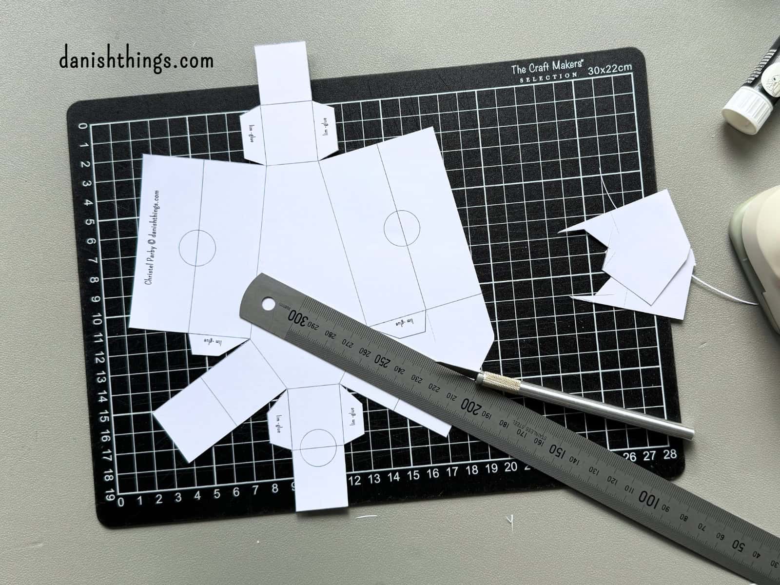 En hvid kistebund ligger på et sort skæreunderlag med en metallineal og en skalpel. De lige linjer kan skæres med hobbykniv eller klippes med en saks.
© Christel Parby · danishthings.com · #DanishThings #HalloweenDIY #Papirklip #GratisPrint