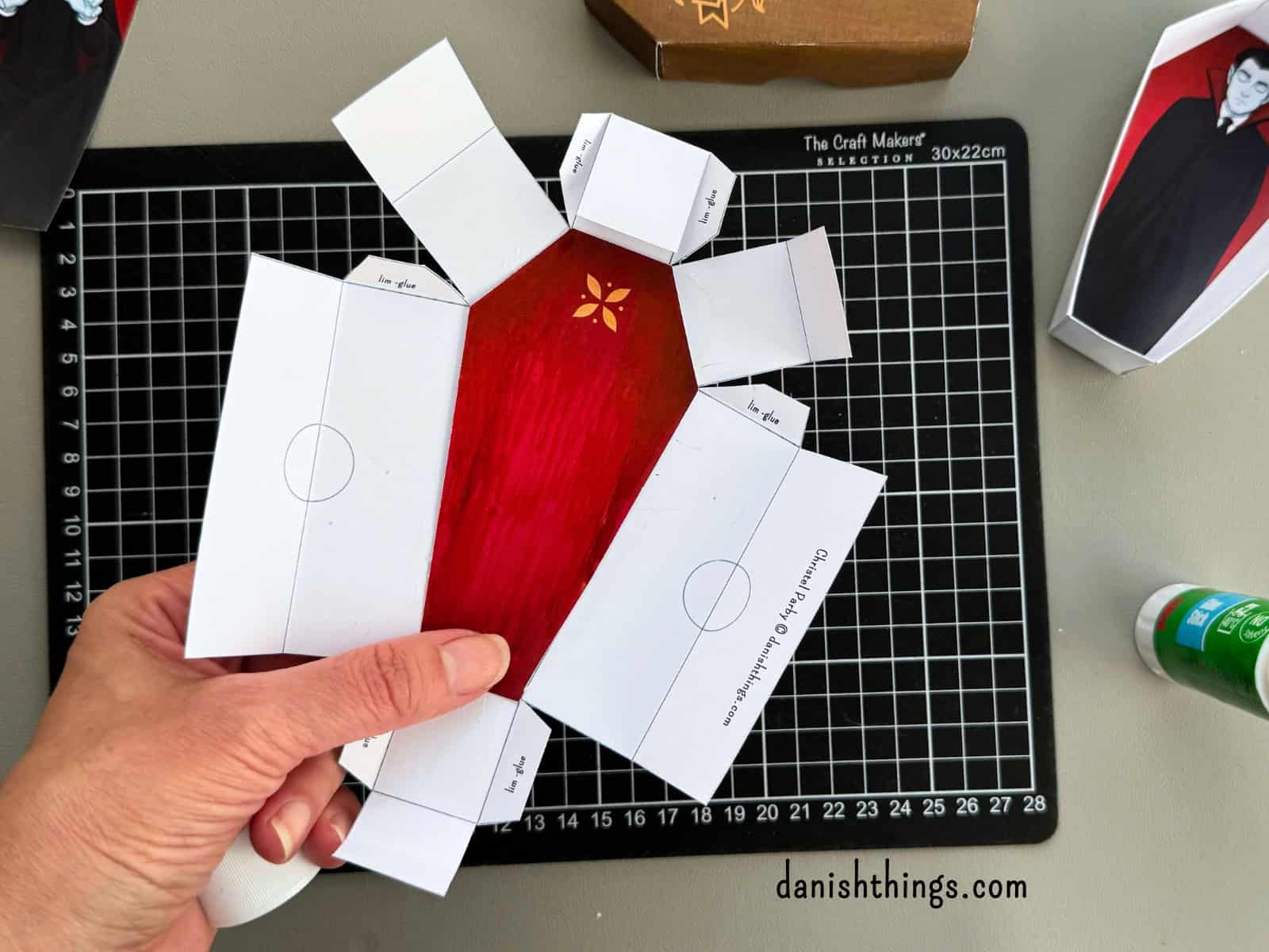 Et udfoldet hvidt kistelåg med et rødt papirindlæg limet på indersiden. Billedet viser, hvordan det røde for kan placeres, før låget samles.
© Christel Parby · danishthings.com · #DanishThings #Kistelåg #HalloweenDIY #GratisPrint
