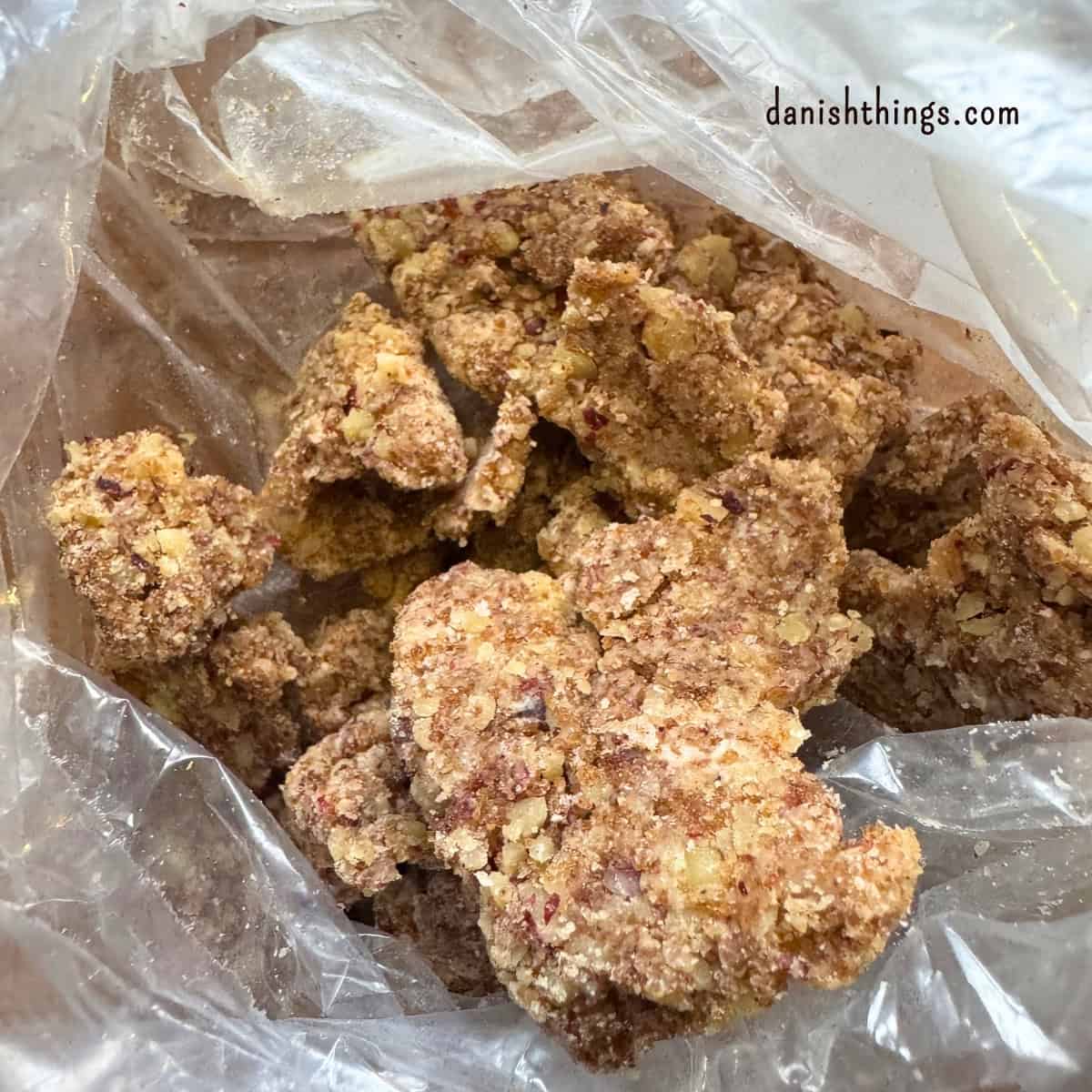 Klumper af valnøddecrumble i en frysepose, klar til at blive fordelt over bananmuffins. Crumblen er lavet med mel, brun farin, hakkede valnødder, smør og kagekrydderi og er kølet ned i fryseren. Find opskriften på Danish Things © Christel Parby #DanishThings #valnøddecrumble #valnødder #muffintopping #crumble #bananmuffins 